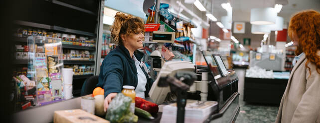 Eine Kassiererin hilft einer Kundin beim Auschecken im Supermarkt. Ein Kassierer hilft einer Kundin beim Auschecken. - JLPSF11901