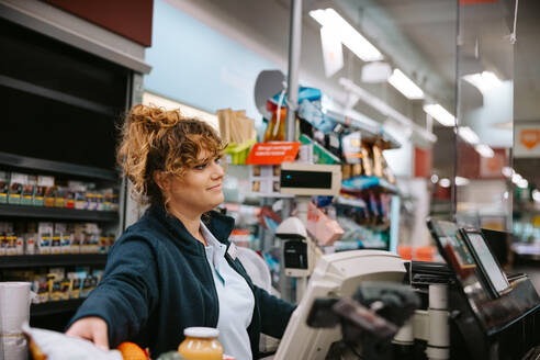Eine Frau arbeitet als Kassiererin in einem Lebensmittelgeschäft und bedient die Kunden an der Kasse. - JLPSF11902