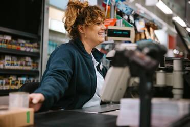 Frau arbeitet an der Supermarktkasse und bedient Kunden. Freundliche Kassiererin arbeitet an der Supermarktkasse. - JLPSF11903