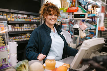 Frau an der Kasse eines Supermarkts, Kassiererin lächelt in die Kamera. - JLPSF11905