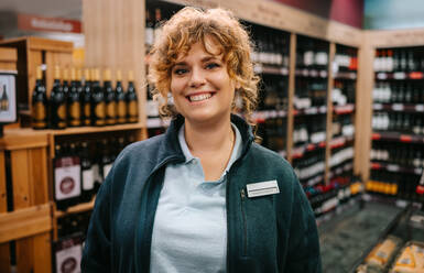 Frau, die in einer Weinhandlung arbeitet. Porträt einer weiblichen Genießerin, die in einer Spirituosenhandlung steht und in die Kamera lächelt. - JLPSF11915