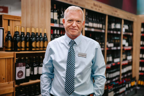 Porträt eines fachkundigen Sommeliers in einer Weinhandlung; der Leiter der Spirituosenabteilung eines Supermarkts schaut in die Kamera. - JLPSF11917