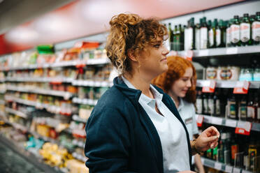 Frau, die mit einer Kollegin im Supermarkt spazieren geht, und der Leiter eines Lebensmittelgeschäfts, der sich die Regale ansieht. - JLPSF11927