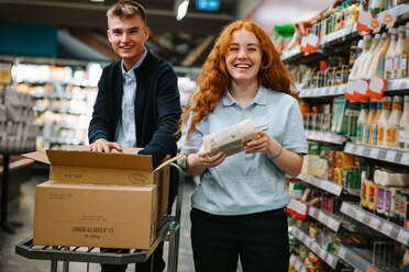 Supermarktangestellte bei der Arbeit im Laden. Männliche und weibliche Angestellte beim Auffüllen der Warenregale im Lebensmittelgeschäft. - JLPSF11929