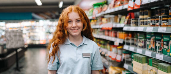 Happy young saleswoman in modern supermarket. Female on a holiday job at grocery store smiling at camera. - JLPSF11936