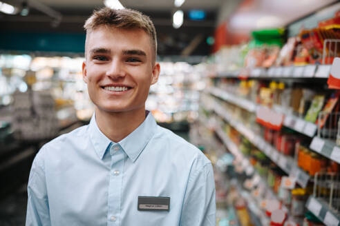 Porträt eines Mannes, der in einem Lebensmittelladen arbeitet. Männlicher Supermarktangestellter, der in die Kamera lächelt. - JLPSF11940