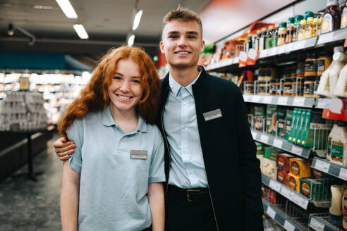 Auszubildende in einem Supermarkt: Mann und Frau stehen zusammen und schauen in die Kamera in einem Lebensmittelgeschäft. - JLPSF11943