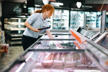 Frau ordnet Fleisch in der Gefriertruhe im Supermarkt. Verkäuferin füllt die Gefriertruhe im Lebensmittelgeschäft auf. - JLPSF11948