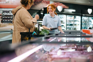 Verkäuferin, die einem Kunden in einem Lebensmittelgeschäft hilft. Junge Mitarbeiterin, die einem Kunden im Supermarkt hilft. - JLPSF11950