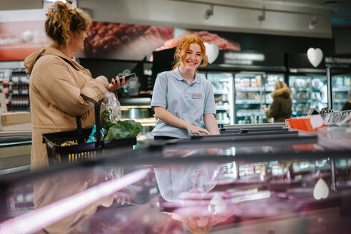 Ein lächelnder Supermarktangestellter hilft einem Kunden im Laden. Ein junger Angestellter hilft dem Kunden in einem Lebensmittelgeschäft. - JLPSF11952