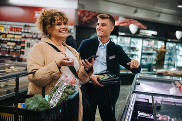 Lächelnder weiblicher Einkäufer mit Assistentin im Lebensmittelgeschäft. Glückliche Frau, die im Supermarkt einkauft. - JLPSF11954