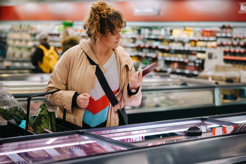 Frau im Lebensmittelladen, die die Etiketten von Lebensmitteln liest. Weibliche Kundin, die im Supermarkt Produktinformationen liest. - JLPSF11955