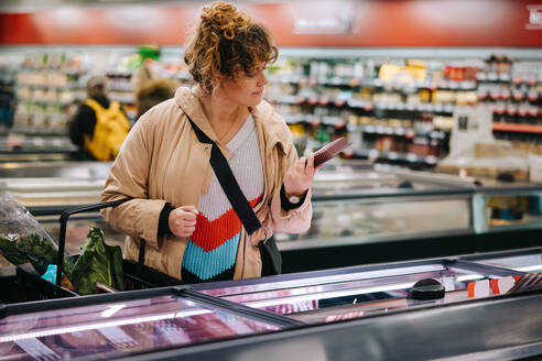 Woman at grocery store reading food labels. Female customer reading product information at supermarket. - JLPSF11955