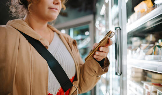 Shopper, der sich die Einkaufsliste auf seinem Handy ansieht. Eine Frau benutzt ihr Handy beim Einkaufen im Supermarkt. - JLPSF11957