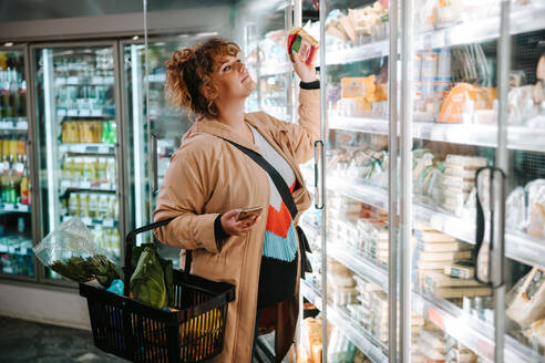 Frau auf der Suche nach dem richtigen Lebensmittel in einem Lebensmittelregal im Laden. Frau kauft Lebensmittel im Supermarkt ein. - JLPSF11959