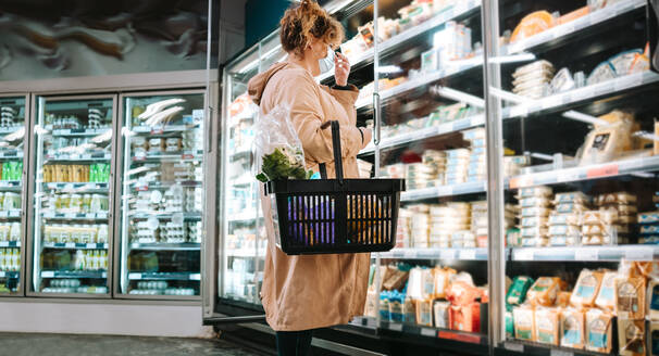 Weibliche Kundin mit Gesichtsmaske in einem Supermarkt. Weibliche Kundin beim Lebensmitteleinkauf während einer Pandemie. - JLPSF11963