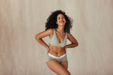 Cozy and comfortable in underwear. Young woman smiling cheerfully while  sitting on the floor in a studio. Confident young woman embracing her  natural body while wearing beige underwear. stock photo