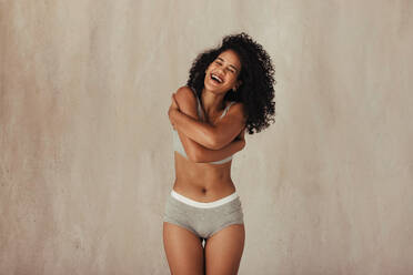 Pretty female model embracing her natural body. Young black woman wearing underwear and smiling with her eyes closed. Woman standing alone against a studio background. - JLPSF11987