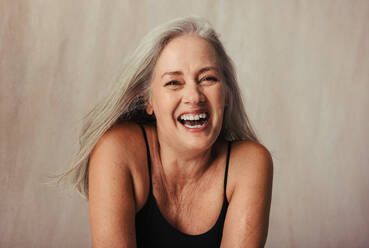 Grey haired woman celebrating her aging body. Body positive woman wearing black underwear and smiling cheerfully. Mature woman posing against a studio background. - JLPSF12039