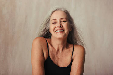 Ältere Frau, die ihren alternden Körper in einem Studio feiert. Körperbewusste Frau, die schwarze Unterwäsche trägt und fröhlich lächelt. Ältere Frau, die vor einem Studiohintergrund posiert. - JLPSF12040