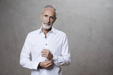 Smiling mature man standing in front of grey background - FMKF07743