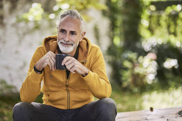 Nachdenklicher reifer Mann sitzt mit Kaffeetasse im Park - FMKF07777