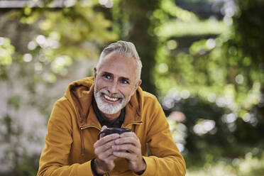 Happy man sitting with coffee cup at park - FMKF07780