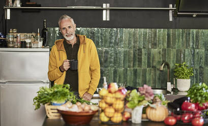 Lächelnder Mann mit Kaffeetasse in der Küche stehend - FMKF07783