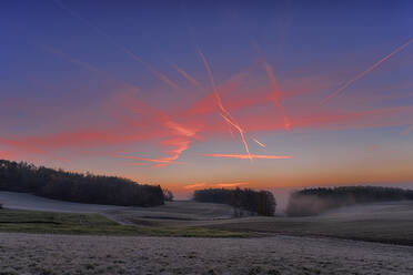 Vapor trails stretching over countryside field at foggy dawn - RUEF03807