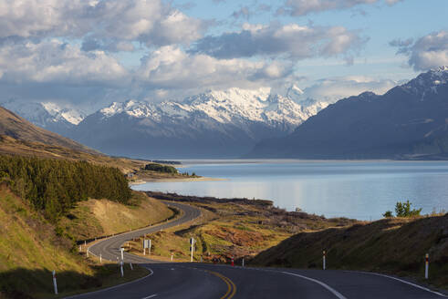 Neuseeland, Canterbury Region, Kurvenreiche Asphaltstraße mit Lake Pukaki und Mount Cook im Hintergrund - RUEF03831