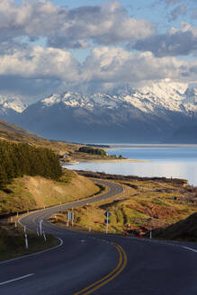 Neuseeland, Canterbury Region, Kurvenreiche Asphaltstraße mit Lake Pukaki und Mount Cook im Hintergrund - RUEF03832