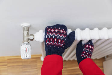 Hands of senior man wearing woolen glove on radiator - GWF07612