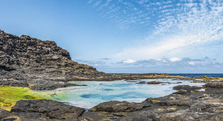 Rough rock formations surrounding pool with clean water on shore of sea against cloudy blue sky in Charcos de los Clicos in Lanzarote, Spain - ADSF39855