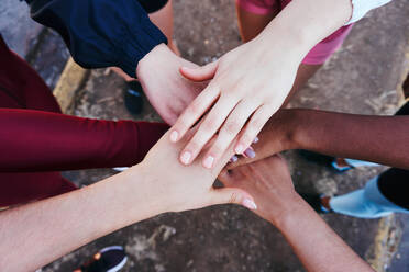 From above team of crop anonymous diverse female athletes stacking hands while standing on sunny day - ADSF39862