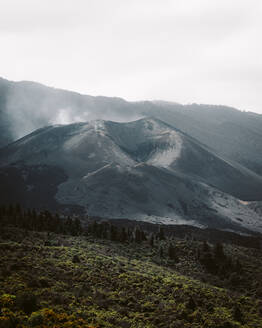 Atemberaubender Blick auf einen schneebedeckten Bergrücken mit Waldbäumen vor einem bedeckten Morgenhimmel in La Palma, Spanien - ADSF39884