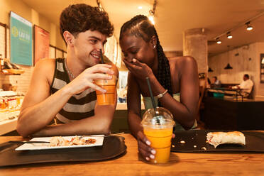 Verschiedene Freund und Freundin mit Tassen frischen Saft lachen über lustige Witze beim gemeinsamen Mittagessen im Restaurant - ADSF39910