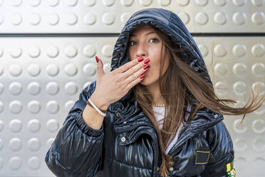 Woman covering mouth with hand in front of metal wall - DLTSF03200