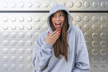Woman with long brown hair wearing hooded shirt in front of metal wall - DLTSF03210