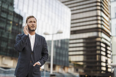 Besorgter Geschäftsmann spricht mit seinem Handy vor einem Gebäude - JCCMF07709