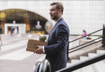 Businessman with cardboard box moving down steps - JCCMF07724