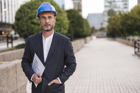 Nachdenklicher Ingenieur mit Schutzhelm auf dem Gehweg - JCCMF07728