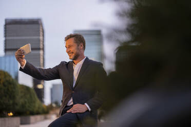 Glücklicher Geschäftsmann spricht Selfie durch Handy in der Stadt - JCCMF07732