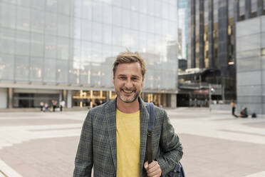 Happy man standing in front of building - JCCMF07743