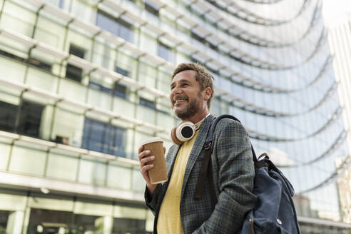 Smiling man holding disposable cup in city - JCCMF07749