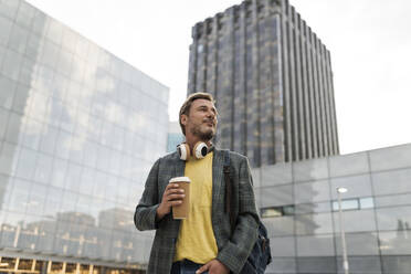 Thoughtful man with disposable coffee cup outside building - JCCMF07752