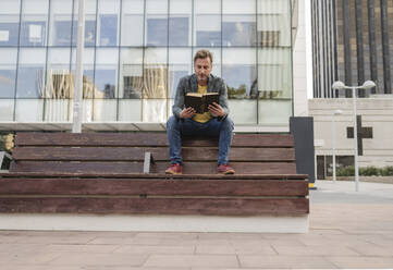 Mann sitzt auf einer Bank und liest ein Buch - JCCMF07757