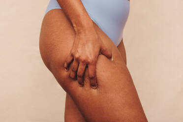Closeup of an anonymous woman grabbing her thigh in a studio. Unrecognizable woman standing in blue underwear against a studio background. Body positive woman embracing her natural body. - JLPSF12096