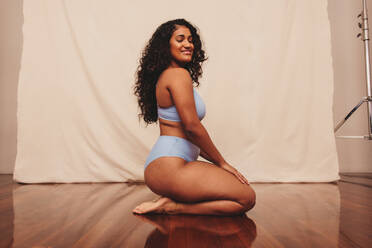 Smiling young woman kneeling in blue underwear against a studio