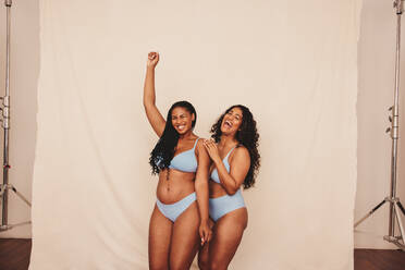Two body positive young women wearing blue underwear in a studio. Two  confident young women embracing their natural bodies and curves. Young women  standing together against a studio background. stock photo