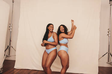 Cheerful young women dancing while wearing blue underwear. Two happy young  women celebrating their natural bodies